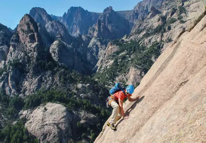 Un grimpeur en plein effort sur un rocher, avec les majestueuses montagnes de Bavella en arrière-plan. L'escalade bavella offre des vues spectaculaires.