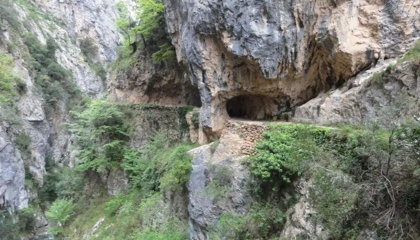 Sentier creusé dans la roche, le long de la ruta del Cares dans les Picos de Europa. Un tunnel naturel s'ouvre sur le chemin.