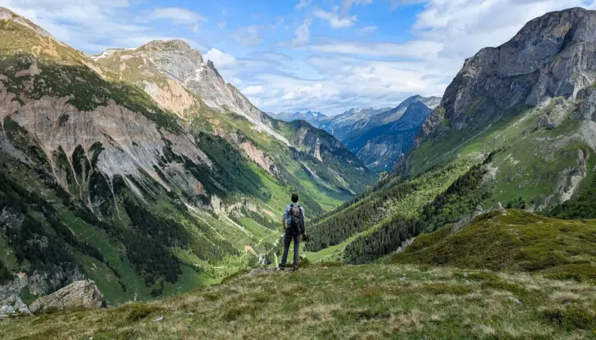 Vue panoramique d'une vallée verdoyante dans le parc de la Vanoise. Un randonneur contemple le paysage, comme sur une carte.