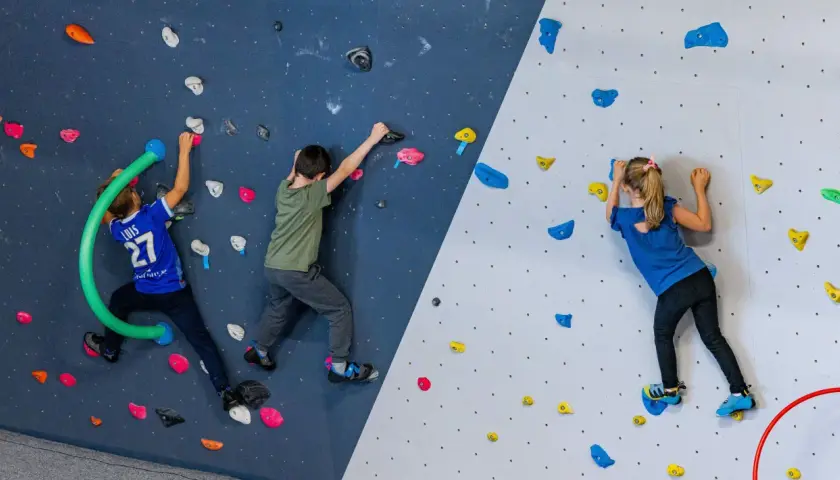 Trois enfants s'amusent lors d'une bloc session à Vienne, grimpant sur un mur coloré avec des prises variées.