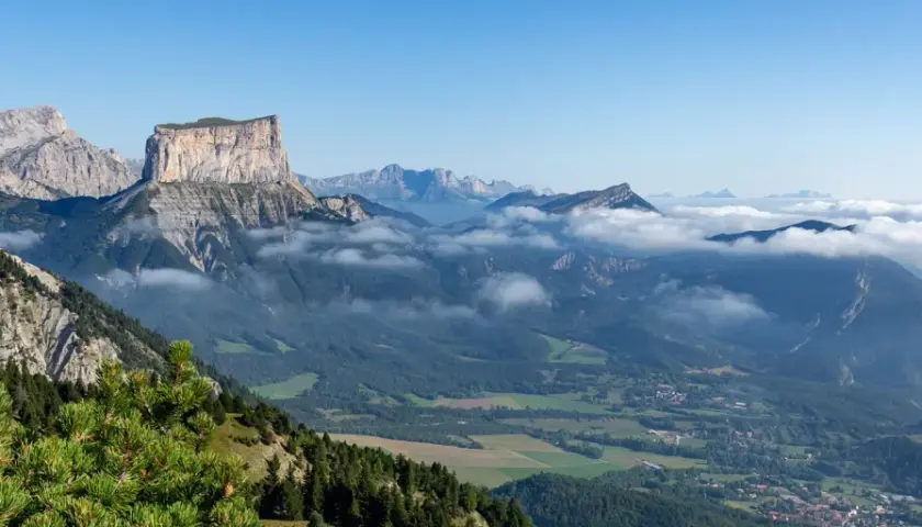 Vue panoramique du Vercors en été. Des montagnes majestueuses, des nuages bas et une forêt verdoyante invitent à explorer ce paysage magnifique.