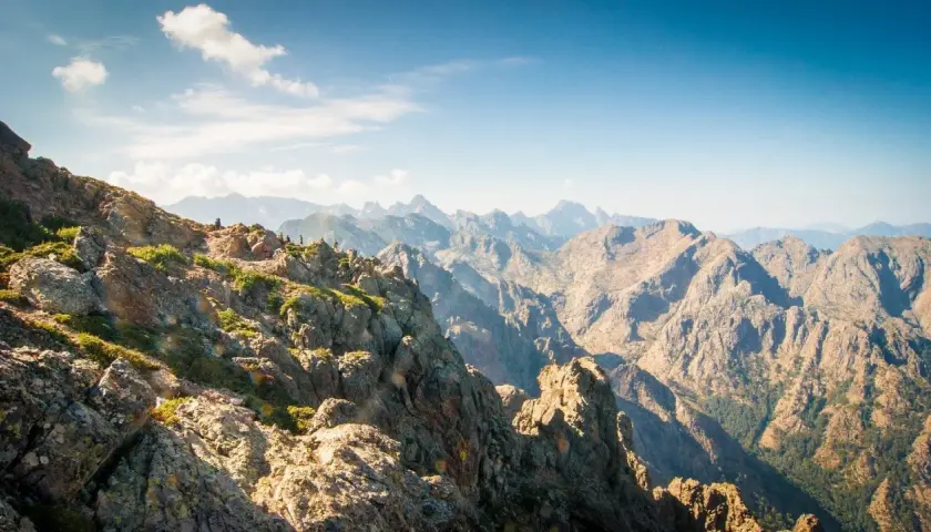 Vue spectaculaire sur la partie sud du GR20, avec des randonneurs sur un sentier rocheux et des montagnes majestueuses à perte de vue.