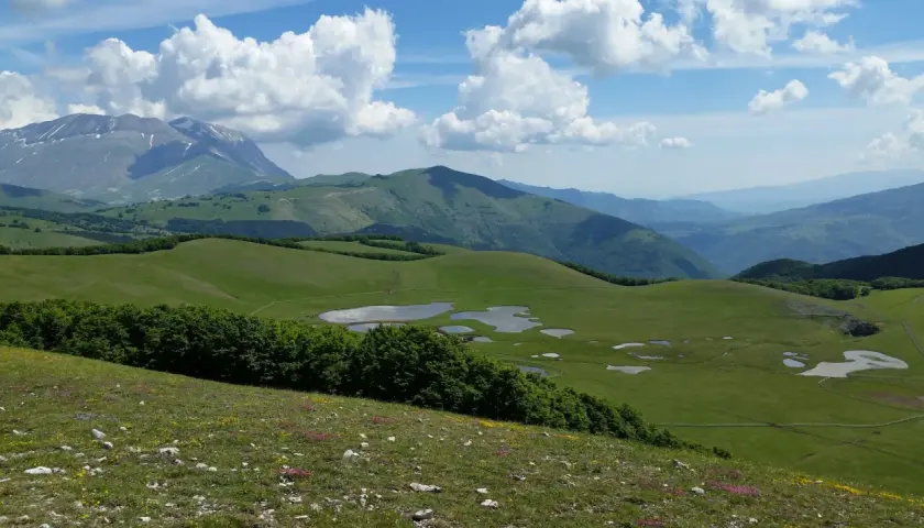 Vastes prairies verdoyantes parsemées de petits étangs dans le parc national des Monts Sibyllins, sous un ciel bleu et nuageux.