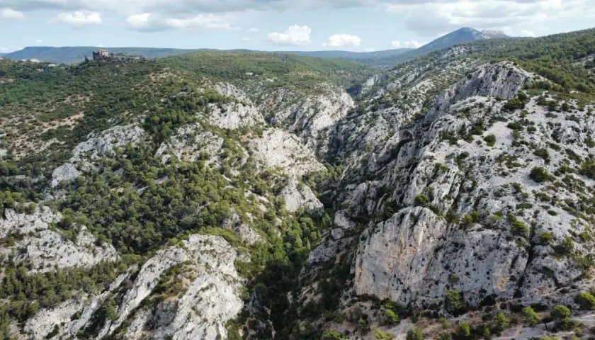 Vue aérienne de la **gorge d'Ollioules**, un canyon rocheux bordé de pins, avec un château en ruines sur une colline au loin.