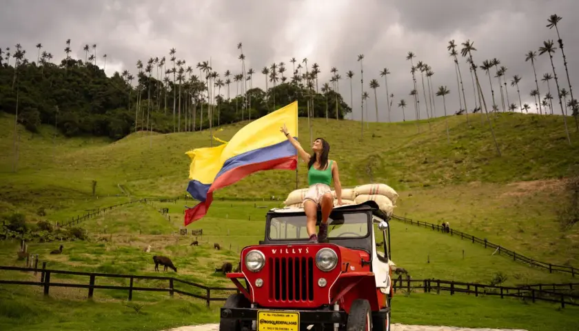 Femme sur une jeep rouge, drapeau colombien flottant, au milieu des palmiers de cire de la Vallée de Cocora, Colombie.