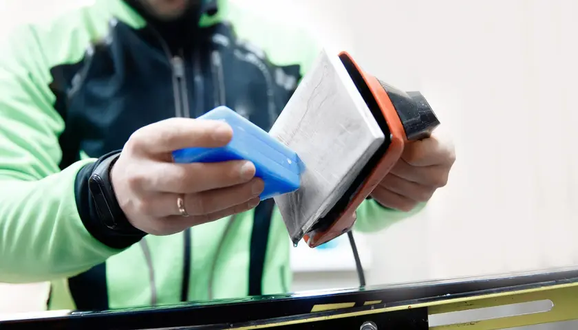 Un skieur prépare ses skis neufs. Il applique de la cire avec un fer chaud, une étape essentielle pour une glisse optimale.