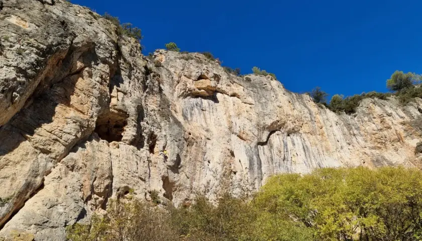 Un grimpeur jaune défie la falaise imposante, un véritable chateauvert pour l'escalade. Le ciel bleu azur surplombe ce paysage rocheux.