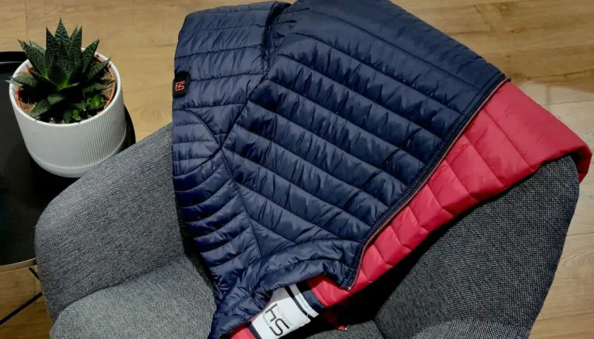 Doudoune bleu marine et rouge pliée sur un fauteuil gris. Une plante verte est posée à côté. Idéal pour redonner du gonflant à une doudoune.