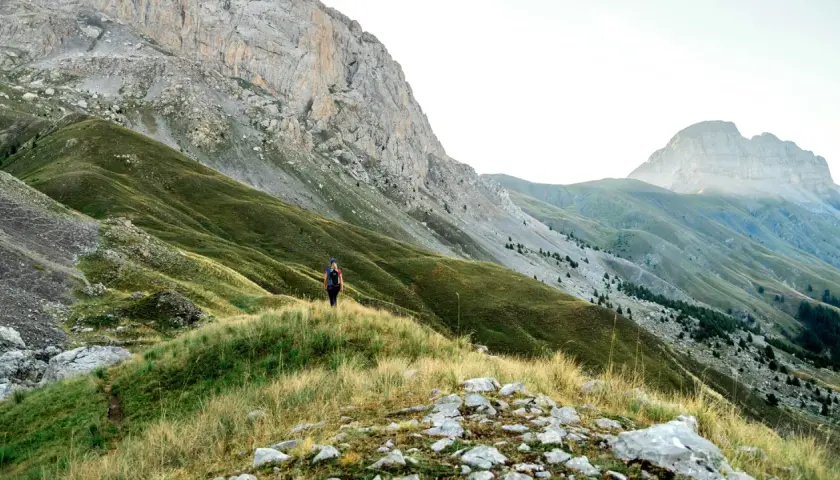 Randonneuse solitaire sur un sentier herbeux, dominant les pentes verdoyantes et les montagnes majestueuses du tour de l'Ubaye.