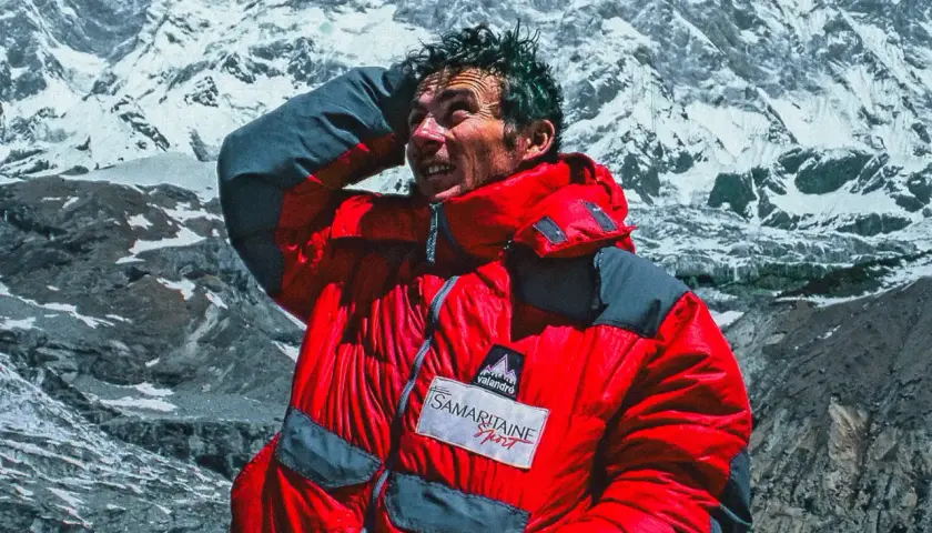 Jean-Christophe Lafaille, le visage marqué par l'effort, se protège du soleil sur fond de montagnes enneigées.