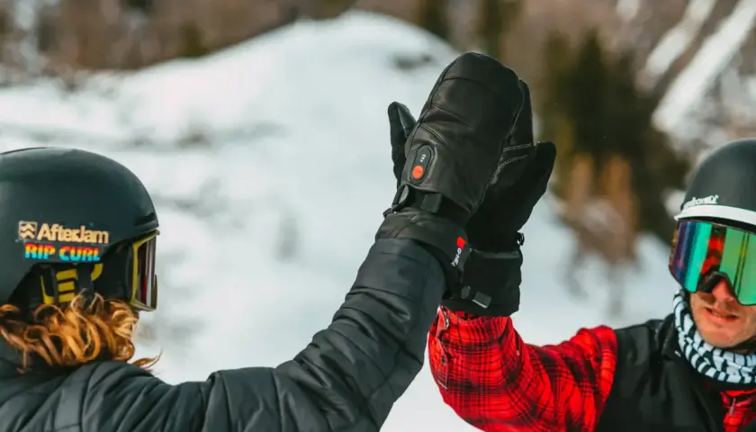 Deux skieurs se donnent une tape dans la main, portant des casques et des lunettes de ski. L'un d'eux a des gants noirs chauffants, une marque de ski de qualité.