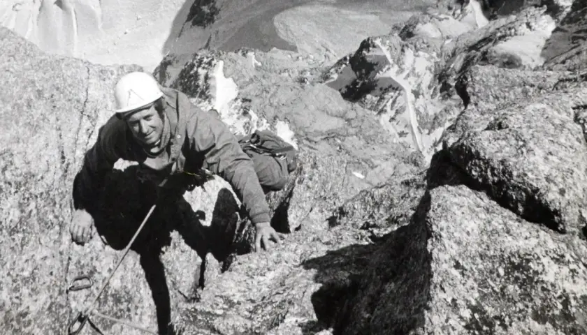Serge Gousseault, alpiniste chevronné, escalade une paroi rocheuse escarpée, casque blanc sur la tête.
