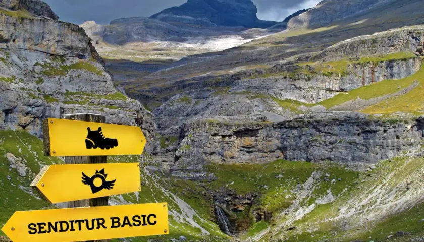Panneau jaune indiquant "SENDITUR BASIC" dans une vallée montagneuse spectaculaire.