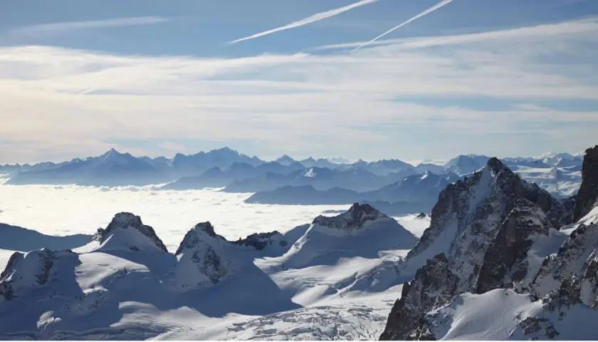 Vue panoramique d'une majestueuse montagne France enneigée, avec des sommets bleutés à l'horizon et une mer de nuages blancs.