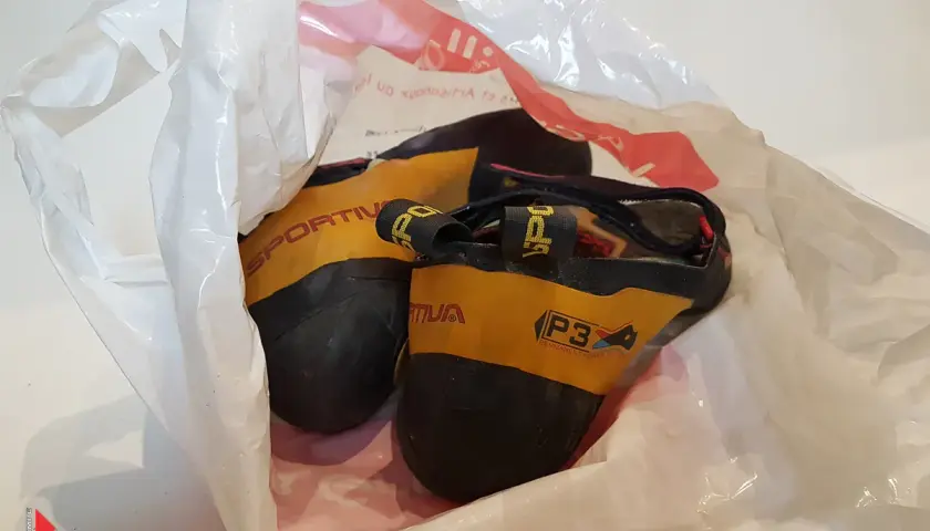Une paire de chaussons d'escalade Sportiva jaunes et noirs, visiblement un chausson qui pue, dans un sac en plastique blanc.