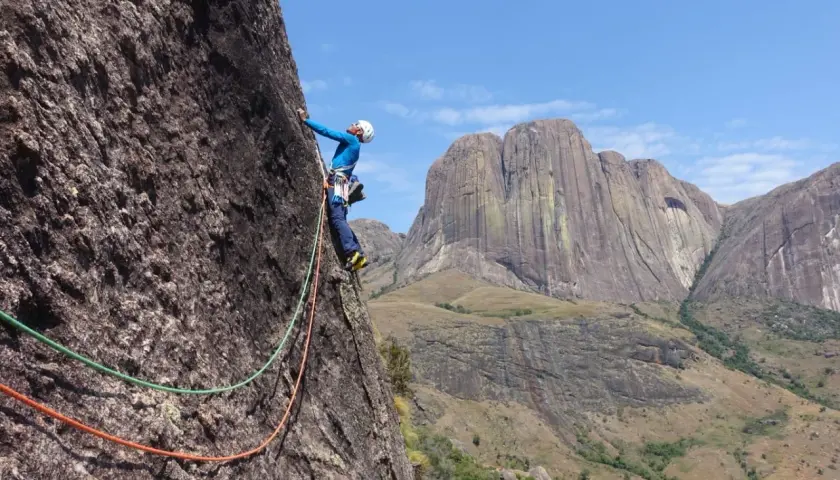 Un grimpeur en pleine ascension sur un rocher impressionnant, avec des montagnes majestueuses en arrière-plan. Une aventure d'escalade à Madagascar.