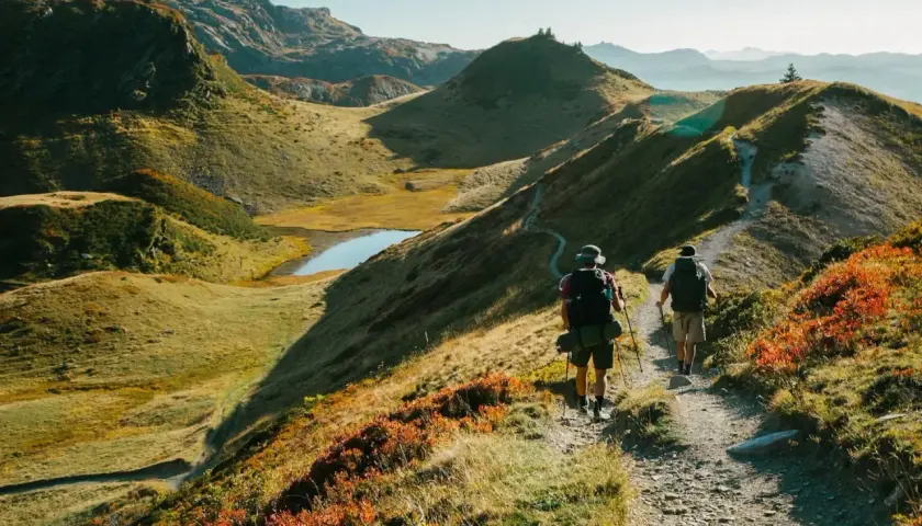 Deux randonneurs avancent sur un sentier de montagne, profitant des paysages spectaculaires. Les couleurs d'automne ajoutent une touche vibrante à la scène, tandis que les fiz s'élèvent au loin.