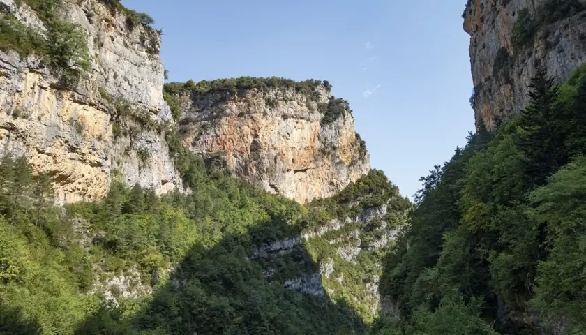 Immenses falaises rocheuses bordent le **Cañon de Añisclo**, couvertes de végétation luxuriante. Le ciel bleu clair domine.