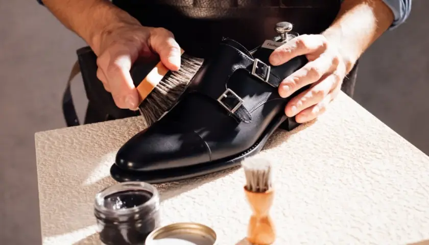 Un artisan brosse une chaussure noire à double boucle, lui redonnant son éclat. La tige de la chaussure est en cuir poli.