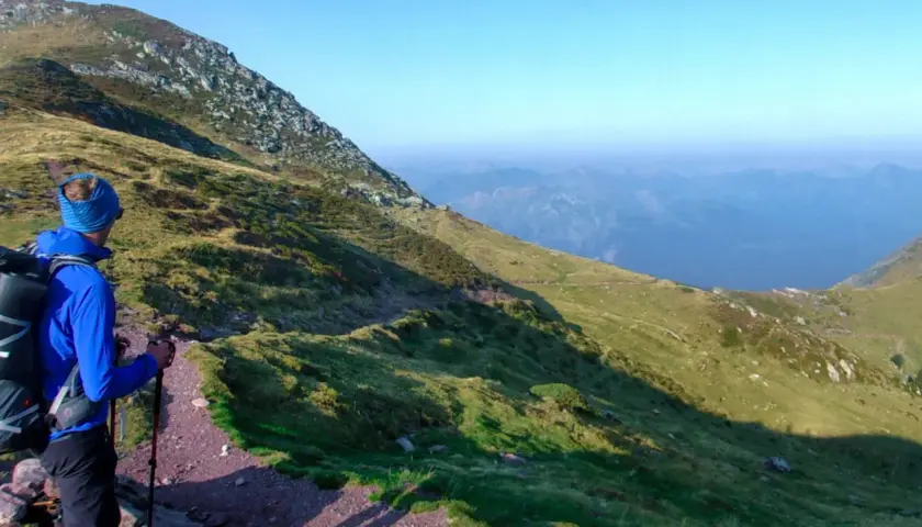 Un randonneur en bleu, prêt pour son premier trek, admire le paysage montagneux.