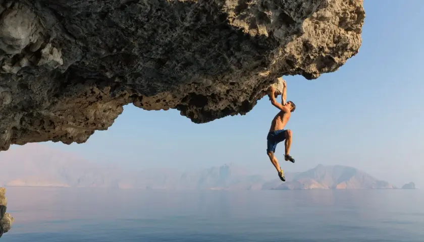 Un homme suspendu à une falaise au-dessus de la mer, une véritable citation escalade pour les audacieux.