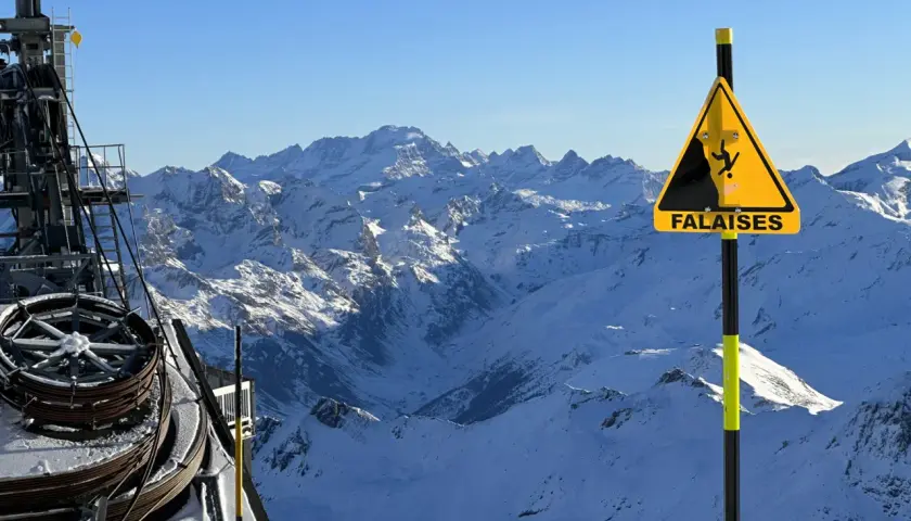 Panneau "Falaises" sur fond de montagnes enneigées, avec une remontée mécanique. Attention aux neiges mouvantes et aux dangers du relief.