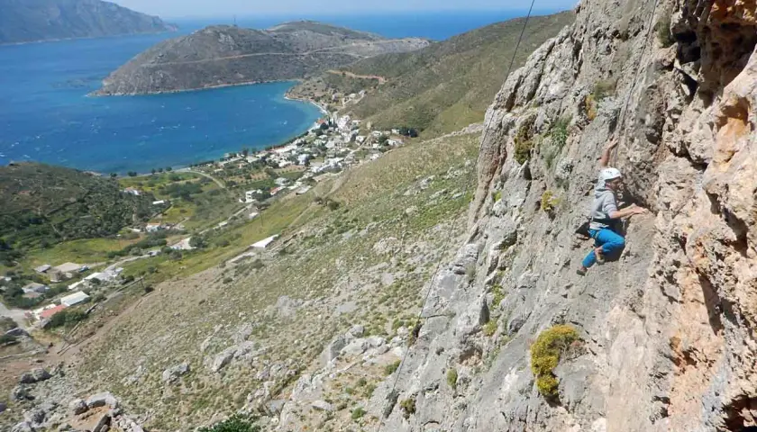 Grimpeur en action sur les falaises de Kalymnos, avec une vue imprenable sur la mer Égée et le village en contrebas.