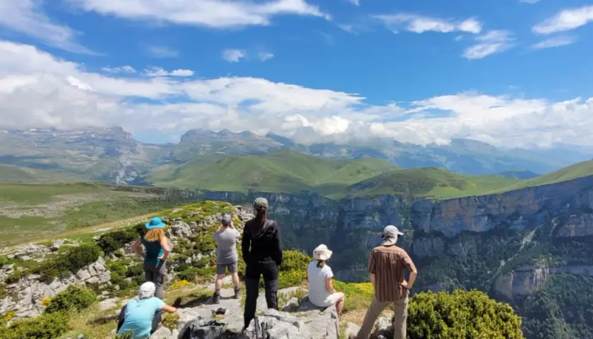 Randonneurs contemplant le paysage spectaculaire du **parque nacional de Ordesa y Monte Perdido**, avec ses falaises abruptes et ses montagnes verdoyantes sous un ciel bleu.