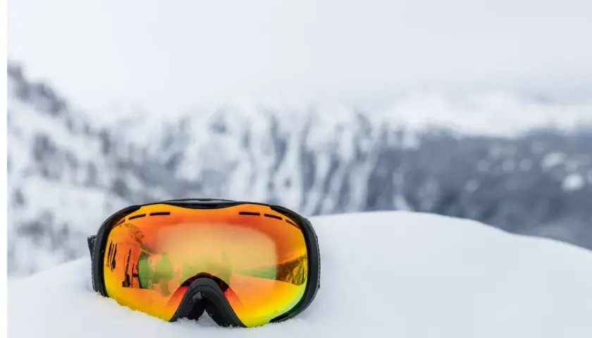 Masque de ski orange posé dans la neige, reflétant des skieurs. Indispensable pour savoir quel masque de ski choisir.