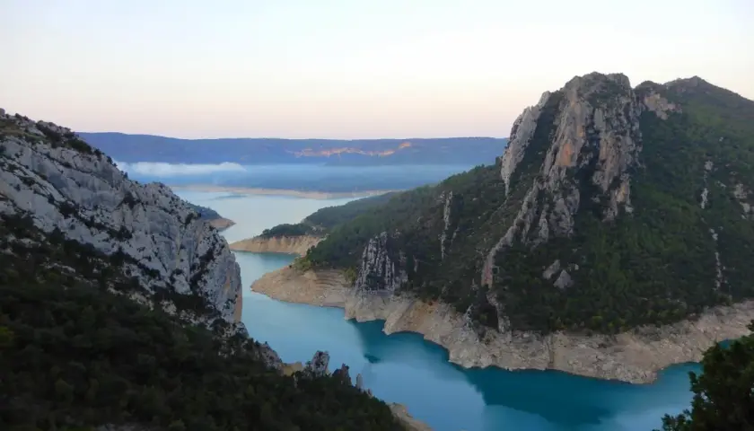 Vue spectaculaire des **pasarelas de Montfalcó** serpentant entre des falaises rocheuses et un lac aux eaux turquoise.