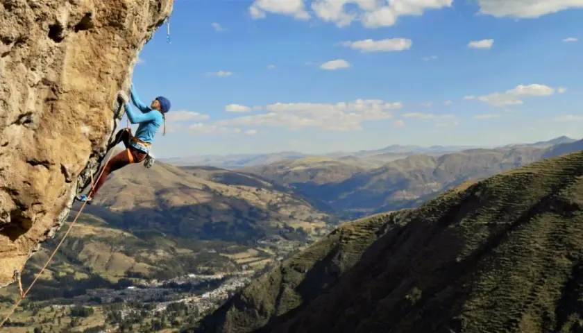 Charlotte Durif, grimpeuse audacieuse, défie la falaise rocheuse sous un ciel bleu. Paysage montagneux spectaculaire en arrière-plan.