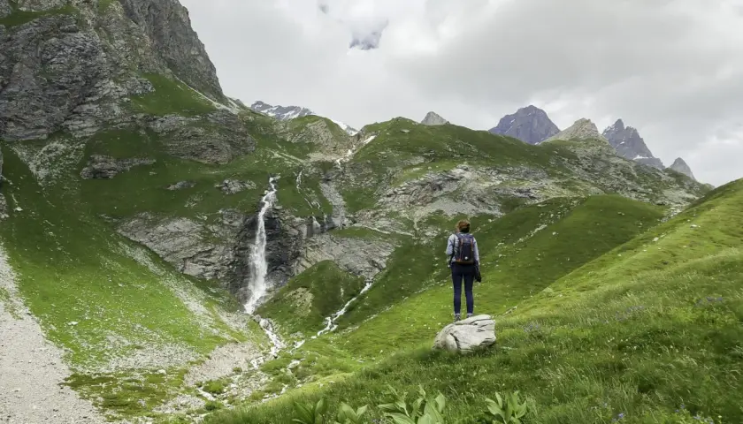 Une randonnée dans les Bauges, avec une cascade impressionnante et des montagnes verdoyantes. Une femme admire le paysage.