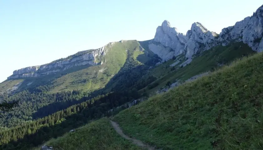 Sentier de randonnée au Col Vert, Villard de Lans. Paysage de montagne verdoyant avec falaises rocheuses et forêt.