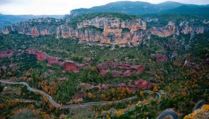 Paysage spectaculaire de falaises rouges et vertes, avec une route sinueuse traversant la vallée. Un paradis pour la siurana escalade.