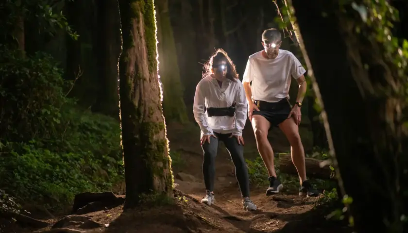 Deux coureurs équipés de lampes frontales s'aventurent sur un sentier forestier sombre. Une **randonnée nocturne** pleine d'adrénaline.