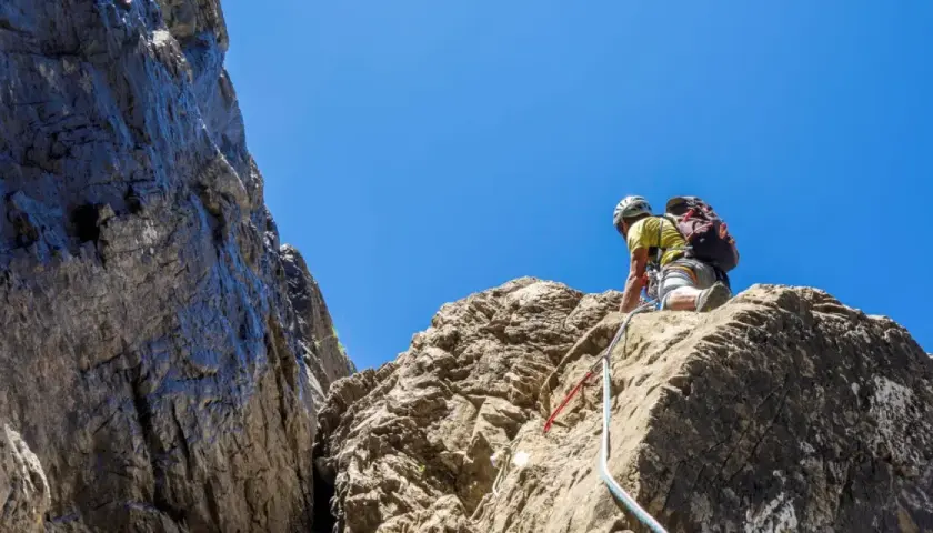 Un grimpeur en plein effort, casque et sac à dos, s'engage sur une paroi rocheuse. L'escalade dans les Pyrénées offre des vues spectaculaires.