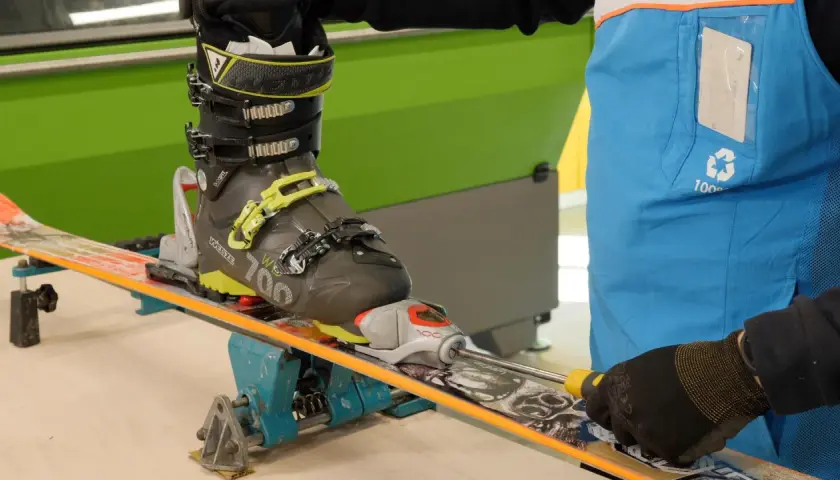 Réglage d'une fixation de ski sur un tableau de fixation. Un skieur ajuste la fixation avec un tournevis.