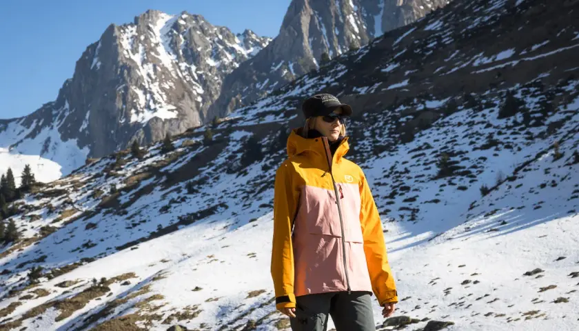 Une femme porte une veste shell colorée, idéale pour affronter les montagnes enneigées.