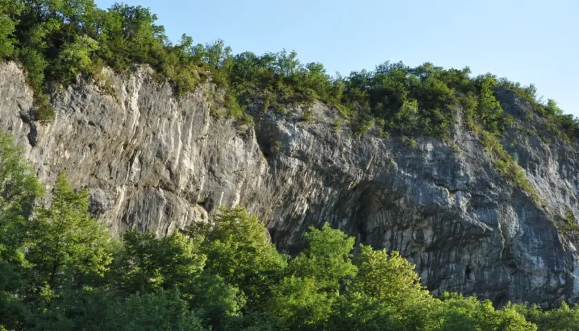 Falaise rocheuse imposante, la balme de Yenne offre un spectacle naturel saisissant, couronnée de verdure sous un ciel bleu.