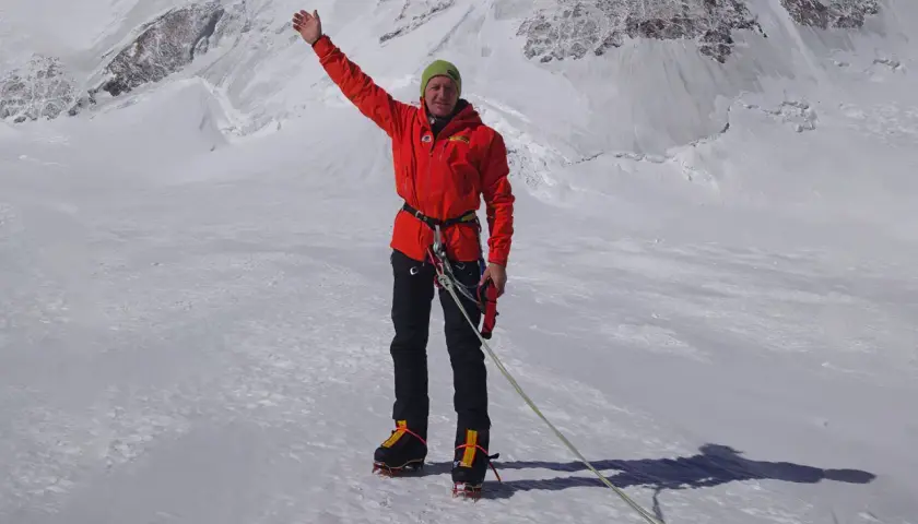 Denis Urubko, alpiniste chevronné, salue depuis un sommet enneigé, prêt pour l'ascension.