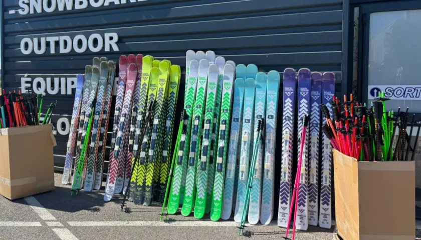 Une rangée de skis de différentes couleurs, certains avec des motifs chevron, prêts pour le freeride. La **taille ski freeride** varie pour s'adapter à tous les riders.