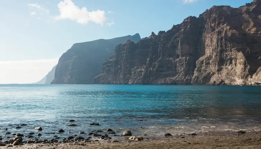 Les falaises de Los Gigantes se dressent majestueusement au-dessus de l'océan bleu. Le rivage est couvert de sable et de galets.