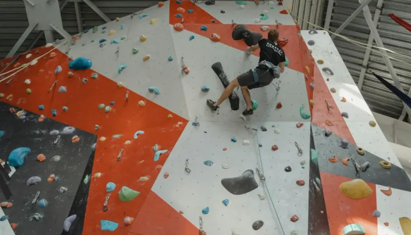 Un grimpeur s'entraîne pour **climb up** sur un mur d'escalade intérieur aux couleurs vives, utilisant des prises variées.