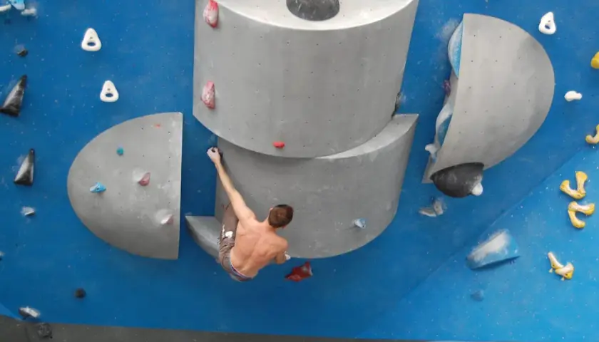 Un grimpeur s'accroche à un bloc escalade, défiant la gravité sur un mur bleu.
