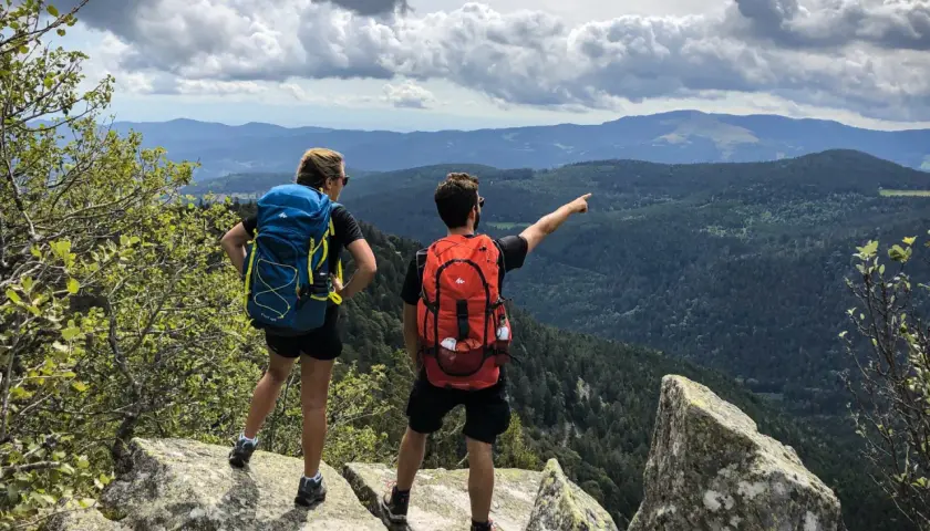 Deux randonneurs contemplent un paysage de montagnes et de forêts. Une balade Vosges facile pour admirer la vue.