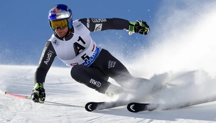 Un skieur acrobatique en plein virage, projetant de la neige avec ses skis rocker. Casque Red Bull, combinaison Colmar.