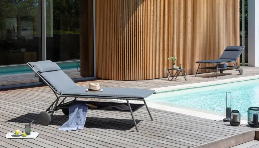 Chaises longues Lafuma près d'une piscine, avec une serviette bleue et un chapeau de paille. Ambiance détente estivale.