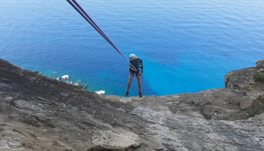 Un grimpeur se prépare pour une descente en rappel au Cap Canaille, avec la mer d'un bleu intense en contrebas. L'escalade offre une vue spectaculaire.