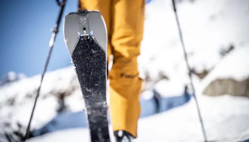 Un skieur en pantalon jaune se prépare à gravir une pente enneigée, sa peau de phoque prête à adhérer à la neige.