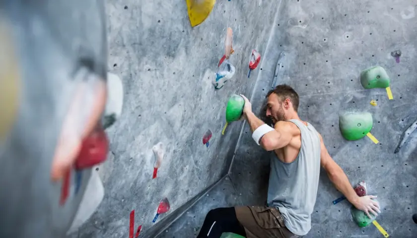 Un grimpeur concentré sur un mur d'escalade, cherchant la prise parfaite. Une scène d'escalade qui pourrait bien finir en humour si la prise glisse !